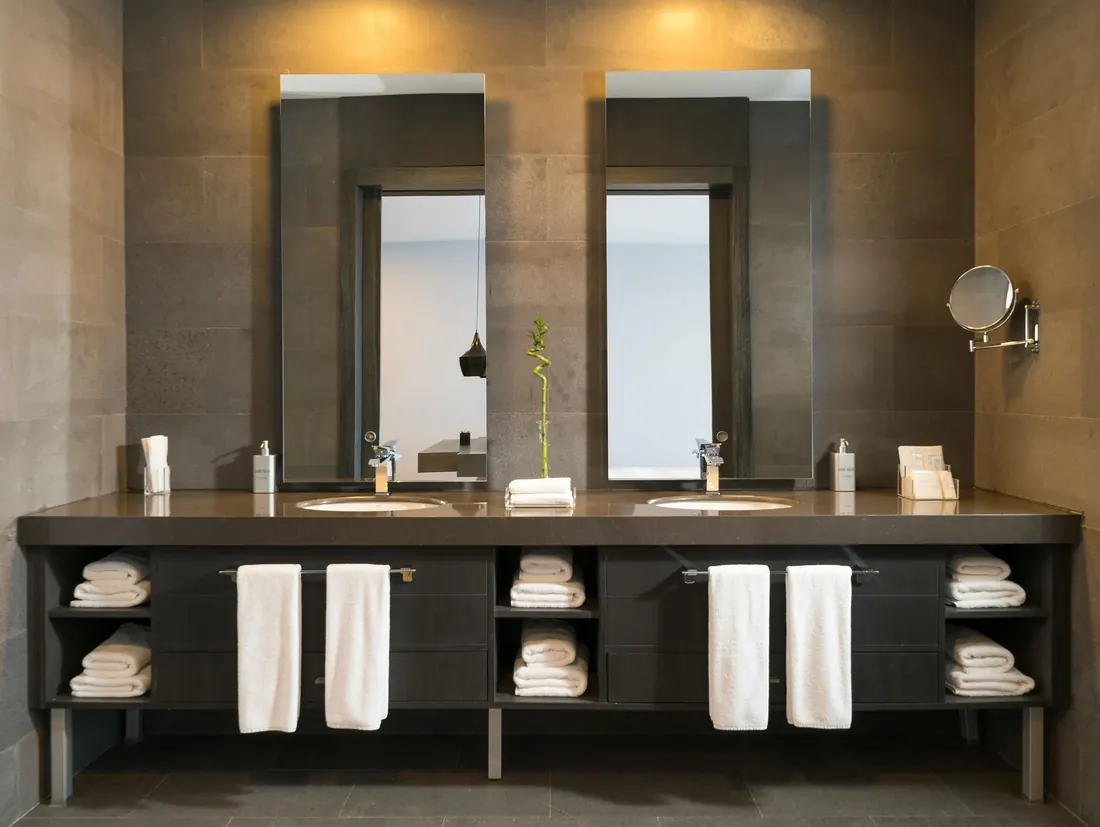 Bathroom with two mirrors, double vanity and folded white towels.