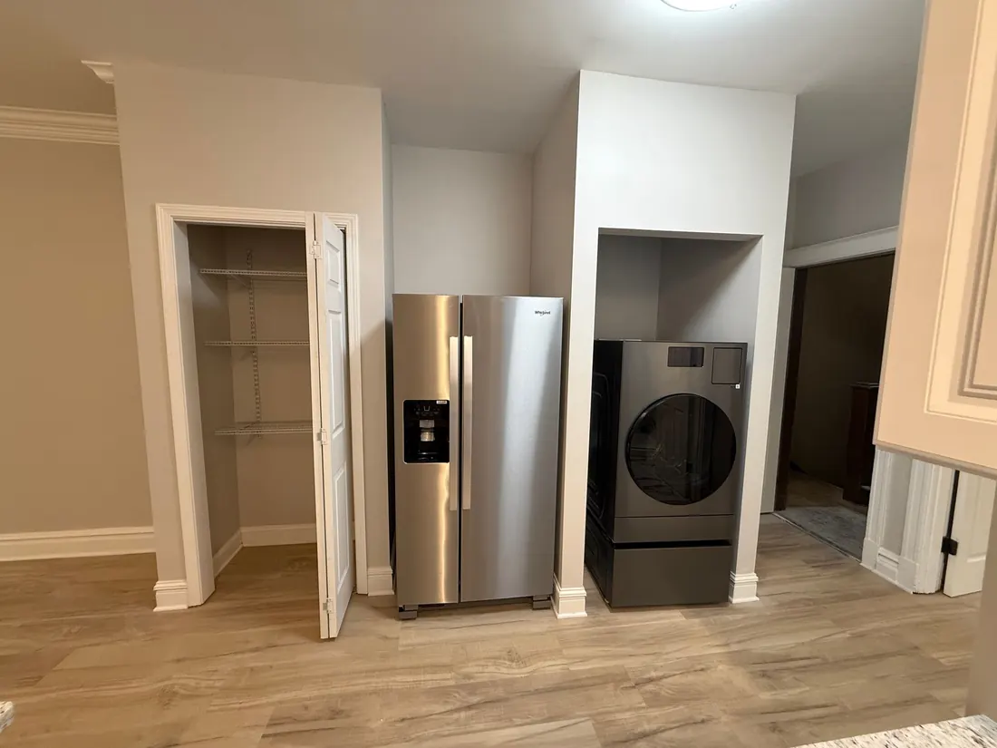 Kitchen area with pantry, refrigerator, and washer/dryer in built-in alcoves. Light wood floors and neutral walls.