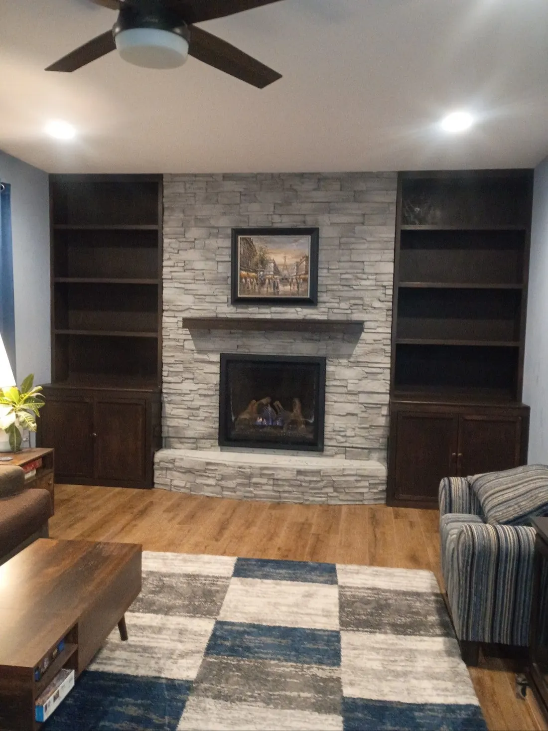 Living room with stone fireplace, built-in bookshelves, wooden mantel, and patterned rug.